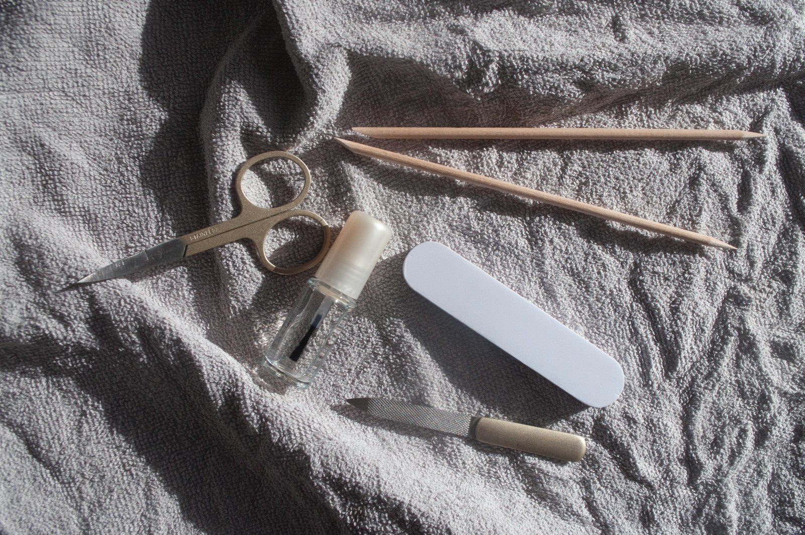 Nail files, scissors, polish and wooden manicure sticks arranged on a towel