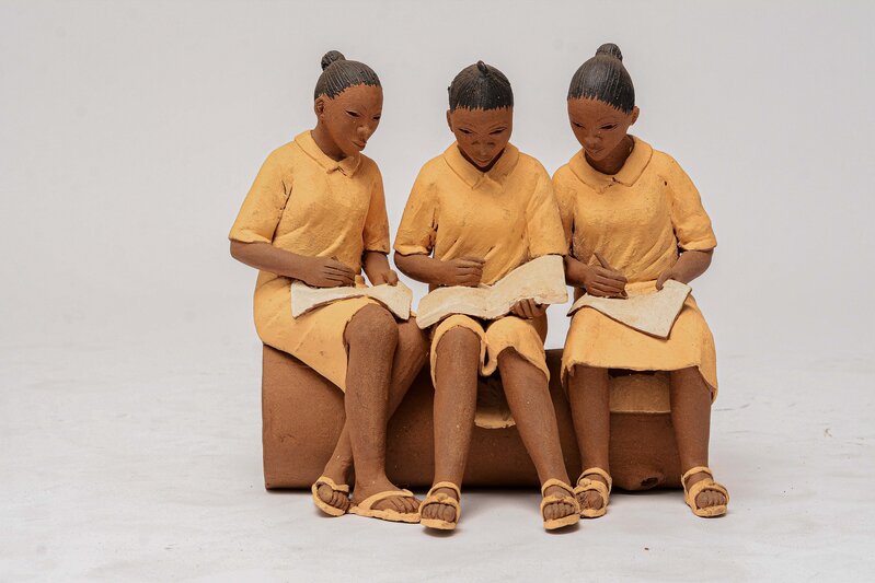 Three terracotta schoolgirls seated closely together and reading