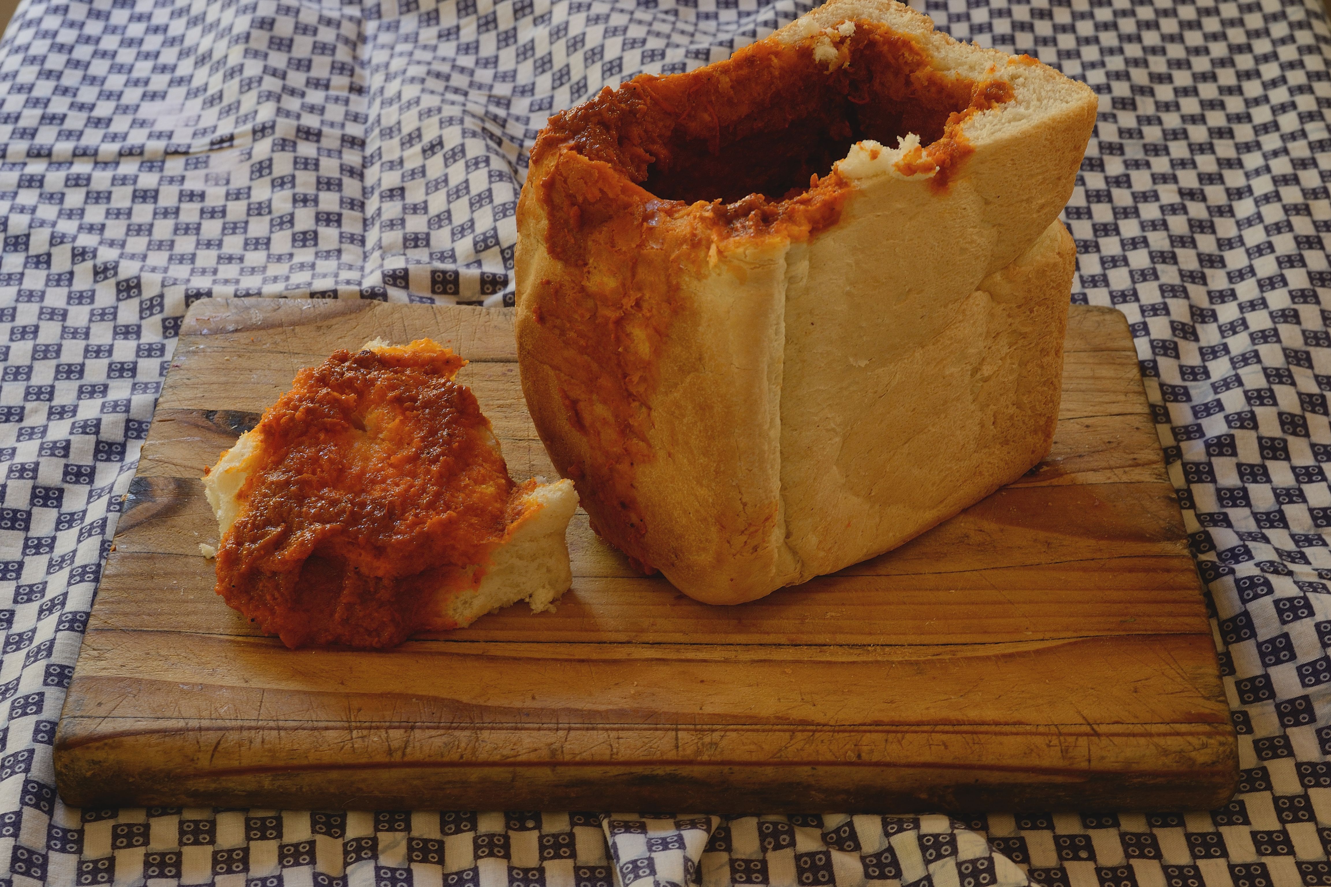 Chicken-curry bunny chow in a hollowed loaf of bread on a wooden board in an archival food photograph