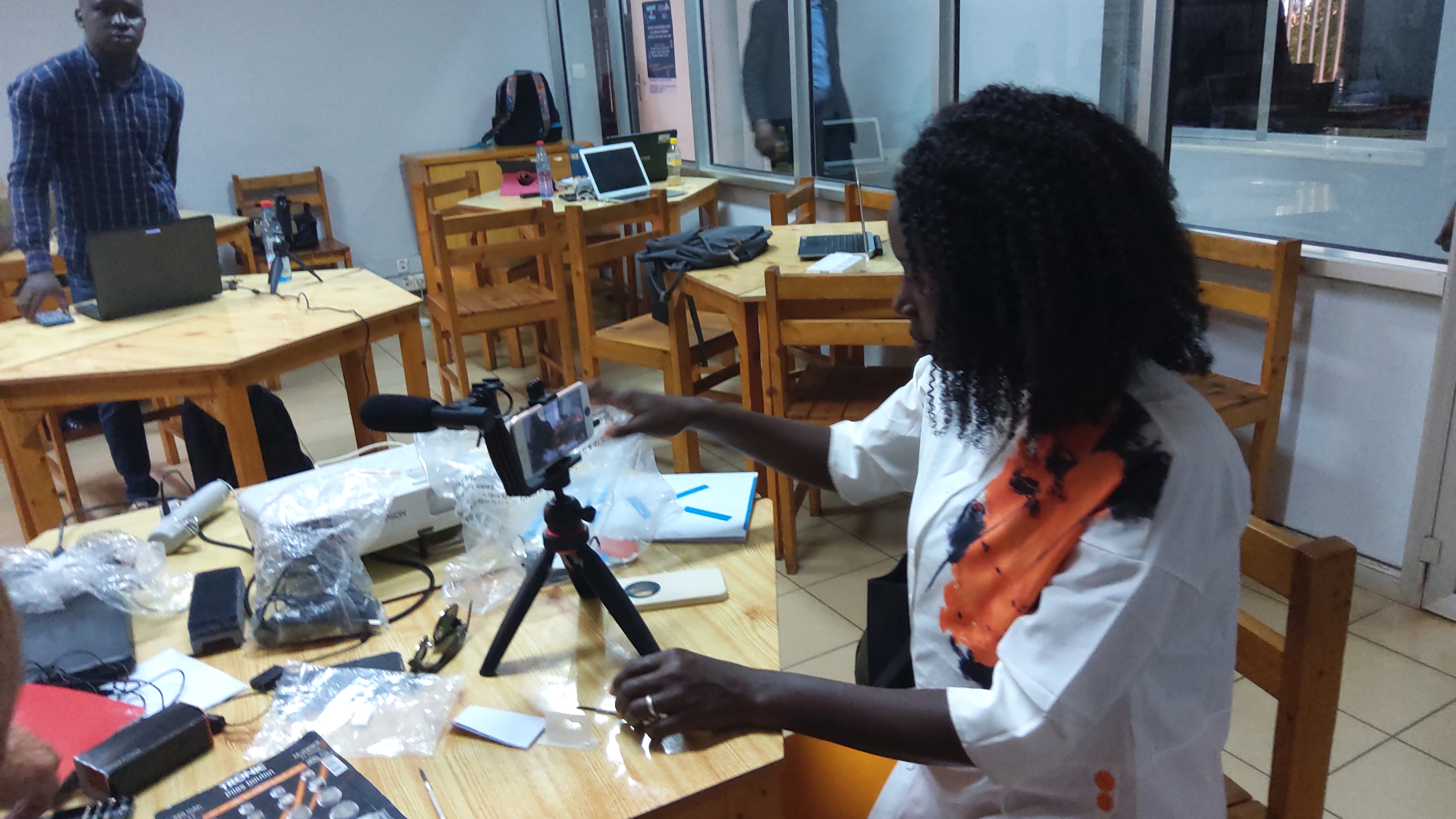 A participant using a phone mounted on a tripod during video-production training in Conakry, with another participant behind her; archive photograph from 2022